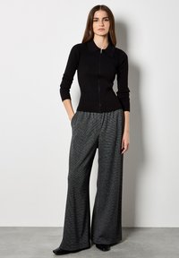 Maglione nero a costine con zip e colletto abbinato a pantaloni a gamba larga grigio a quadri. Entrambi i capi sono aderenti e rifiniti.