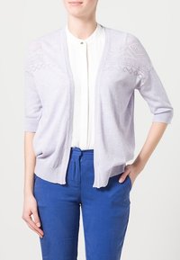 Ljus lavendelfärgad cardigan med öppen framsida, korta ärmar och intrikat spetsdesign på axlarna. Matchas med vit blus och blå byxor.