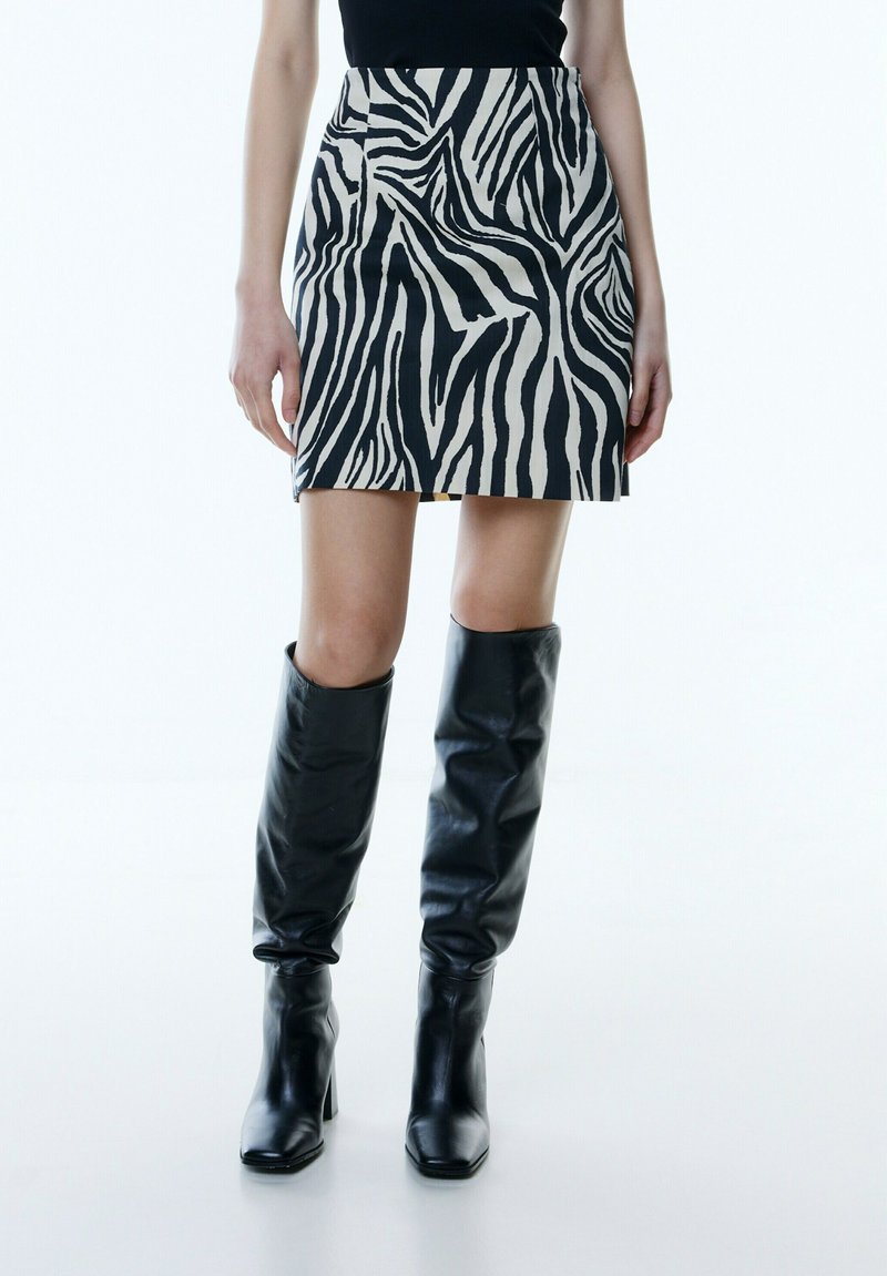 Miniskirt met zebrapatroon in zwart en crème, gemaakt van een soepele stof. Gecombineerd met hoge zwarte leren laarzen met een strak ontwerp.