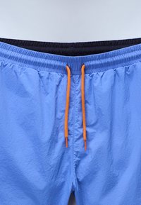 Costum de baie bleu cu un tiv elastic, căptușeală interioară neagră și șnur portocaliu. Țesătură texturată cu o finisare netedă.