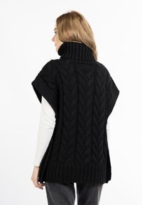Schwarzer gestrickter Poncho mit hohem Kragen, der ein strukturiertes Zopfmuster aufweist. Lockere Passform mit kurzen Ärmeln und einem gerippten Saum am unteren Ende.