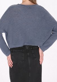 Pull court en maille bleue avec un tissage texturé, associé à une jupe en denim noire taille haute avec poches arrière et finition lisse.