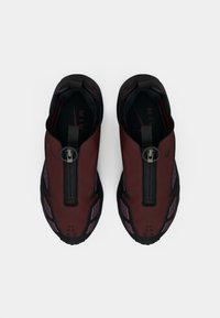 Par tenisica Nike Air u tamnocrvenoj i crnoj boji sa prednjim zatvaranjem na patent zatvarač i ljubičastim detaljima, prikazanih odozgo na bijeloj pozadini.