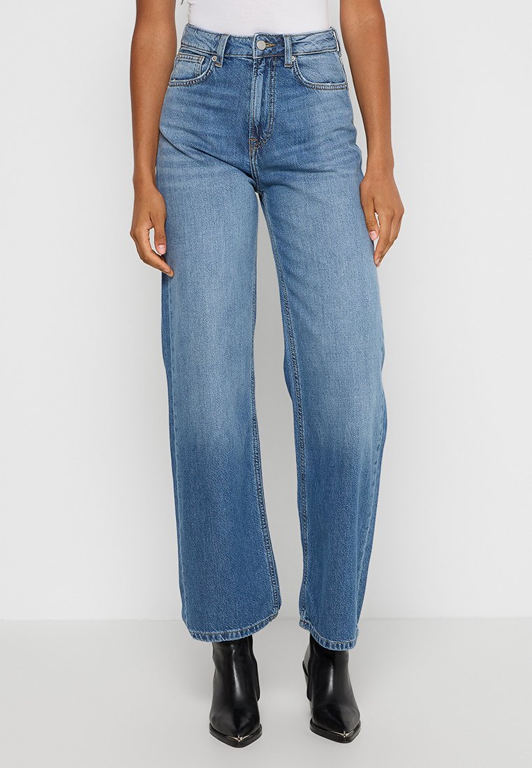 Jasnoniebieskie dżinsy z wysokim stanem o luźnym kroju, z pięcioma kieszeniami i delikatnym przecieraniem, zestawione z czarnymi botkami za kostkę.