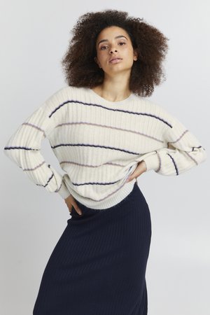 Pull côtelé blanc avec des rayures navy et lilas clair, présentant des manches longues et une coupe décontractée, associé à une jupe côtelée navy.