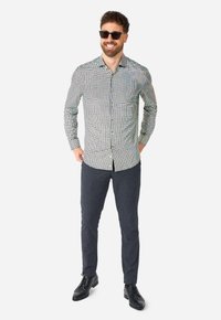 Schwarz-weißer karierten Hemd mit langen Ärmeln, Button-Down-Kragen und blauen strukturierten Hosen. Schwarze Lederschuhe runden das Outfit ab.