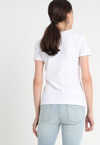 Camiseta de algodón blanca de manga corta, diseño ajustado y escote redondo; se lleva con jeans de mezclilla azul claro.