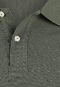 Close-up van een olijfgroene polo met een gestructureerde stof, kraag, knopening en twee witte knopen, waarvan er één vastgemaakt is en de ander open.