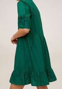Robe en coton vert à manches courtes, jupe plissée et ourlet à volants. Présente des poignets boutonnés et une silhouette classique.