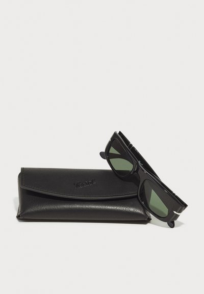 Ochelari de soare negri cu lentile verzi, cu o formă rectangulară elegantă și accente argintii, așezați pe un toc texturat din piele neagră.