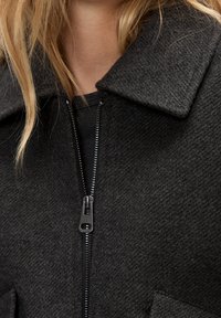 Veste en laine gris foncé avec fermeture éclair à l'avant, col large et tissu texturé, dotée d'une fermeture éclair lisse et de grandes poches plaquées.