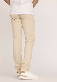 Pantalons en coton beige avec un design fuselé, tissu légèrement élastique et texture lisse, associés à des baskets blanches et beiges.