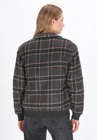 Grå rutmönstrad tröja med röd och svart checkmönster, tillverkad av mjukt material. Har ribbad nederkant och ärmar, visad från baksidan.