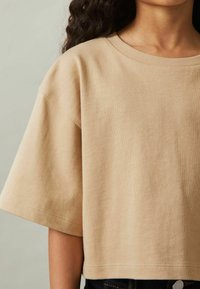 Beige cropped t-shirt med korte ærmer, lavet af blødt tekstureret stof, med rund halsudskæring og lige kant.