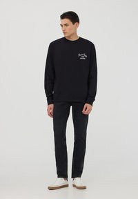 Felpa nera con maniche lunghe, collo rotondo e ricamo bianco. Abbinata a jeans neri e sneakers bianche. Design semplice e casual.
