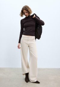 Beżowe spodnie o szerokich nogawkach połączone z obcisłym ciemnym golfem, do tego czarna kurtka, na neutralnym tle.