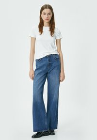 Hvid ribbet kortærmet skjorte parret med brede blå denim jeans. Jeansene har høj talje og kontrastsyninger. Sorte sko fuldender outfittet.
