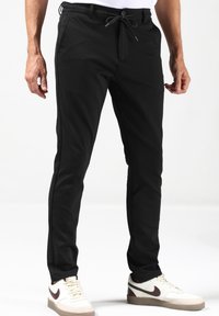 Zwarte broek van een glad, rekbaar materiaal met een koord in de taille, slim fit en zijzakken, gecombineerd met witte sneakers.