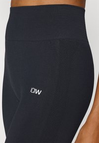 Black leggings with a ribbed high waistband and textured side panels. Features a white "ICIW" logo on the left thigh.