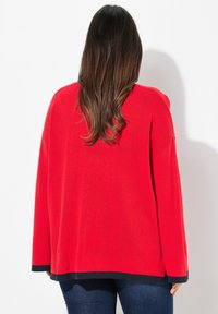 Maglione rosso a maglia con vestibilità morbida e maniche lunghe. Presenta un orlo e dei polsini blu navy. Texture liscia, senza motivi visibili.