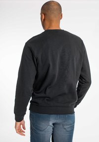 Sudadera negra de manga larga, con cuello redondo y puños acanalados. Llevada con jeans de mezclilla azules, mostrando una textura de tela suave.