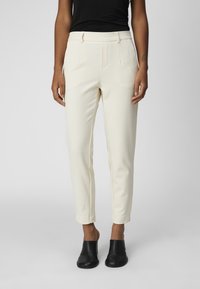 Lys kremfargede bukser med slim fit, flat front, frontlommer og avsmalnende ankler, båret sammen med svarte mules.