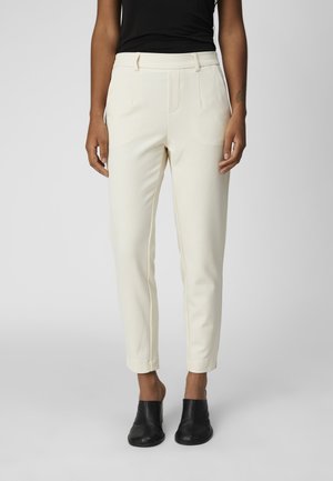 Light cream, tailored trousers with a slim fit, flat front, front pockets, and tapered cuffs, paired with black mules.
