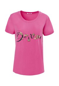 Camiseta de algodón rosa con mangas cortas, que presenta adornos que deletrean "Divino" en negro con acentos decorativos. Textura suave.