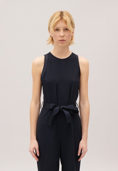 Combinaison sans manches bleu marine avec un buste ajusté, une taille ceinturée et une texture de tissu lisse. Design minimaliste sans motifs.