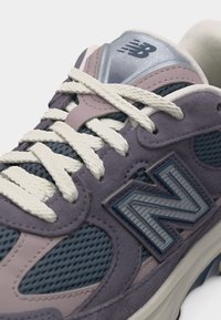 Gros plan sur une basket New Balance bleue et violette avec des lacets blancs et des détails en tissu mesh.