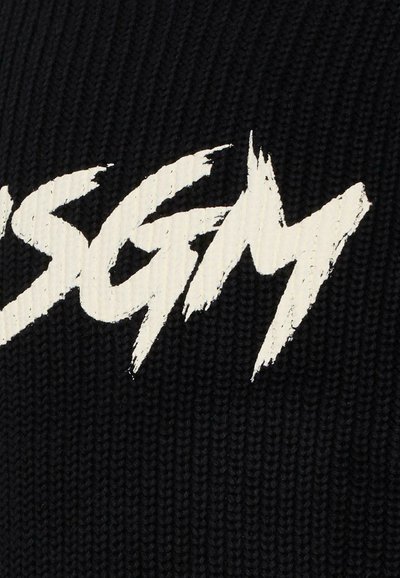 Bonnet en tricot noir avec un grand logo au design en coup de pinceau blanc. La texture semble côtelée et douce.