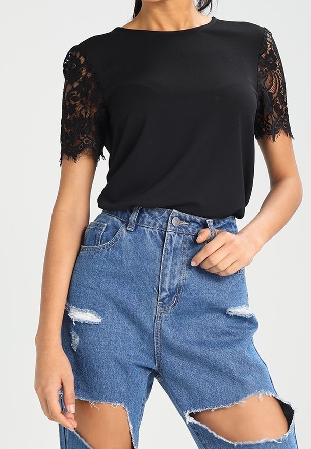 Sort top med blonderærmer, parret med højtaljede blå distressed jeans med store udskæringer og frynsekanter.
