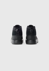 Paire de bottes UGG noires vues de l'arrière, avec une languette de traction et un cordon de serrage au col de la cheville, dotées de semelles en caoutchouc épaisses.