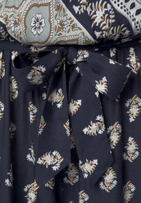 Marinblått tyg med ett blommönster i vita och ockragula toner, med en knytning i midjan och mjuk, texturerad fall.