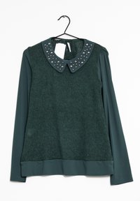 Groene langemouwen trui met een gestructureerd gebreid lichaam, gladde mouwen en een gestofeerde kraag met zilveren accenten. Hangt aan een zwarte haak.