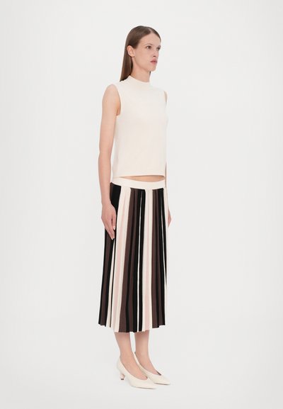 Nude sleeveless top with a high neckline paired with a black, brown, and cream striped pleated skirt and light-colored heeled shoes.