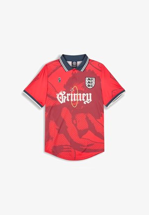 Red polo shirt featuring a large graphic pattern, "Grimey" logo, and crest on the left chest. It has a navy collar and striped accents.