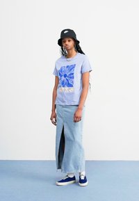 Light purple T-shirt with blue floral design paired with a long denim skirt featuring a front slit. Model wears a black bucket hat and blue sneakers.