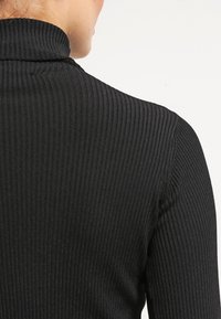 Svart ribbad polotröja med en åtsittande design, vertikal textur och hög krage, visad bakifrån.