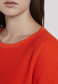 Suéter texturizado rojo con un diseño de canalé, con un amplio cuello redondo y mangas cortas, mostrando detalles alrededor del cuello y la zona de los hombros.