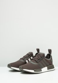 Brown mesh sneakers with gray accents, white soles, and three signature stripes. Features a padded collar and textured rubber sole.