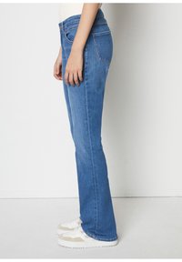 Blå denim med utsvängt ben och medelhög midja, försedda med fram- och bakfickor, diskreta sömmar och i kombination med vita sneakers.