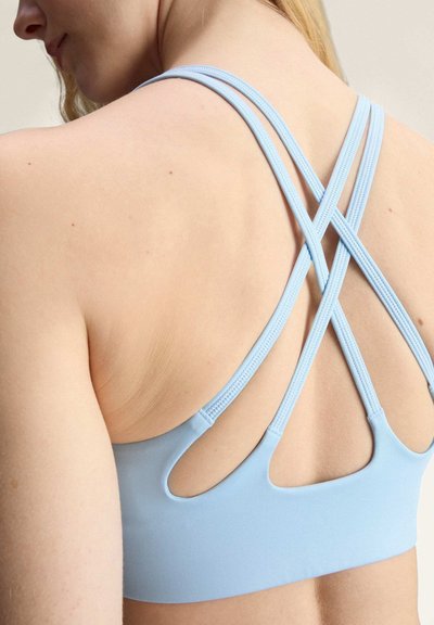 Woman wearing a light blue sports bra with thin, crisscrossed back straps and cutout details near the lower back.