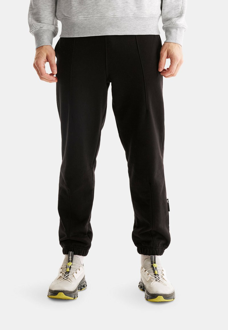 Svarta joggingsbyxor med en smalnande design, tillverkade av ett mjukt material. Har sidofickor och elastiska muddarna. Kombineras med ljusa sneakers.