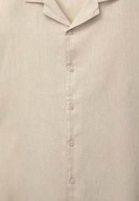 Beige linnen overhemd met een camp collar en vijf beige knopen aan de voorkant, met details van textuur en stof.