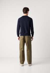 Mornarska pulover z dolgimi rokavi, v kombinaciji s svetlo olivno zelenimi hlačami. Hlače imajo dva zadnja žepa z gumbi.