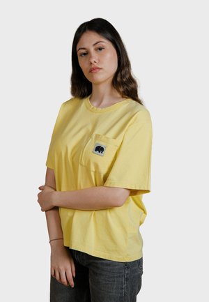Gelbes Baumwoll-T-Shirt mit einer Brusttasche auf der linken Seite, die mit einem Elefant-Graphic gestaltet ist. Kurze Ärmel, lockerer Schnitt und ein einfacher Halsausschnitt.