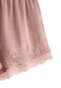 Ljust rosa tyg med blommig spetskant längs nederkanten, som visar delikata sömmönster på en slät textil.