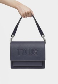 Borsa a spalla in pelle textured blu navy con logo "TOUS" in rilievo, dotata di una patta superiore e di un design a doppio manico per versatilità.