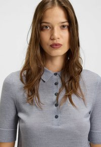 Polo shirt azzurro chiaro a maniche corte realizzato in tessuto morbido, con colletto e sei bottoni scuri lungo la parte anteriore.